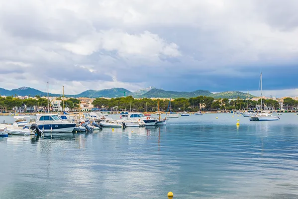Barcos en un puerto tranquilo con monta&ntilde;as y cielo nublado al fondo.