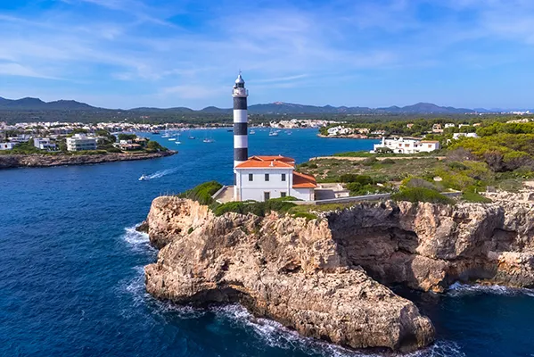 Faro en un acantilado sobre el mar, con paisajes y edificaciones al fondo.