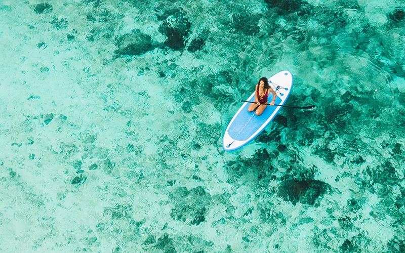 Persona en tabla de paddle en agua turquesa vista desde arriba.