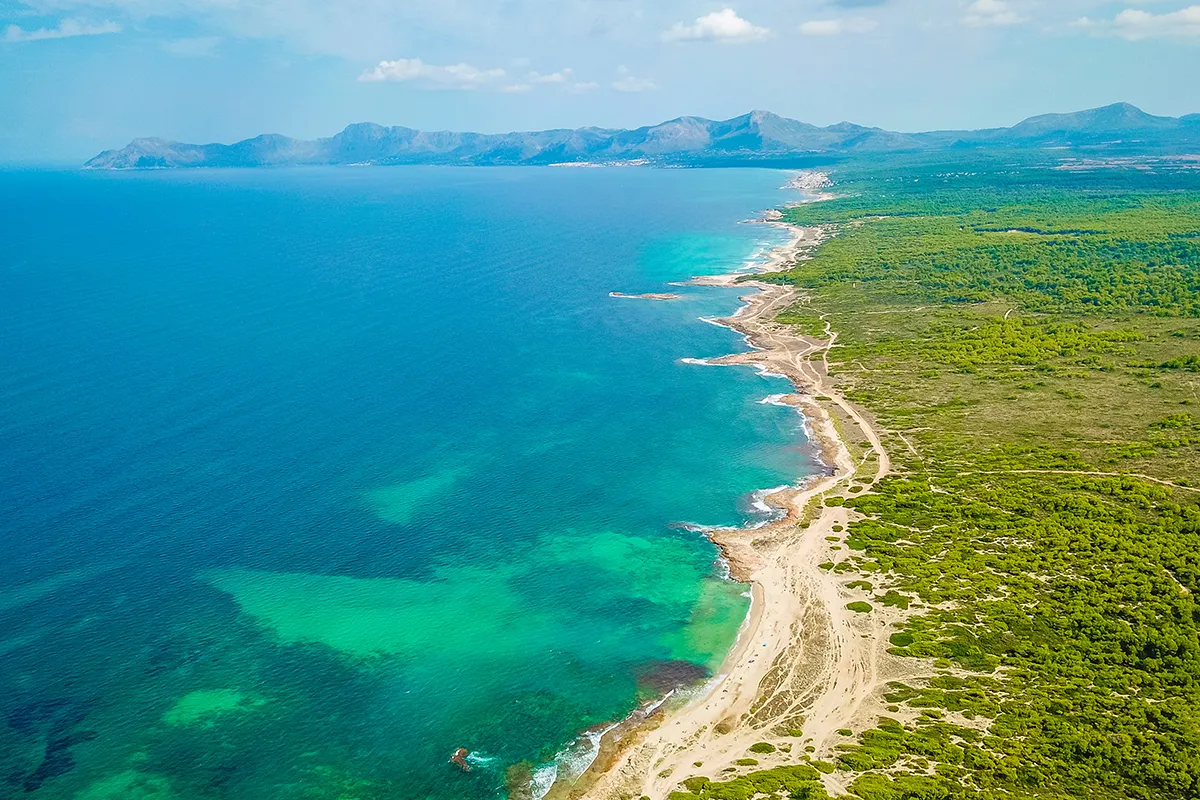 Costa con mar azul y monta&ntilde;as al fondo bajo un cielo despejado.