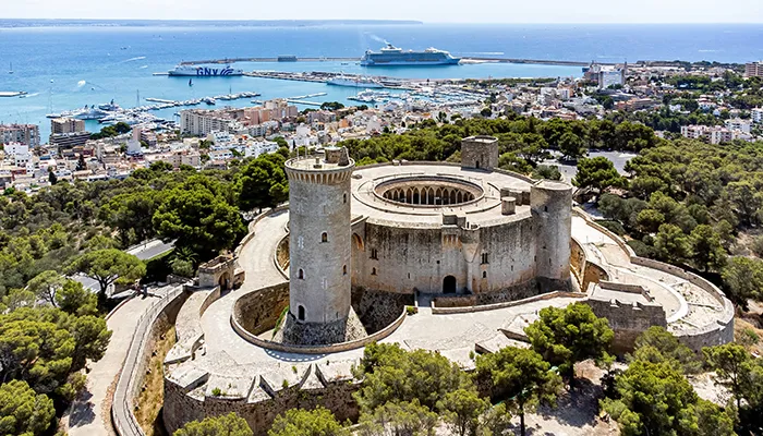 Castillo rodeado de &aacute;rboles con vista al mar y la ciudad al fondo.