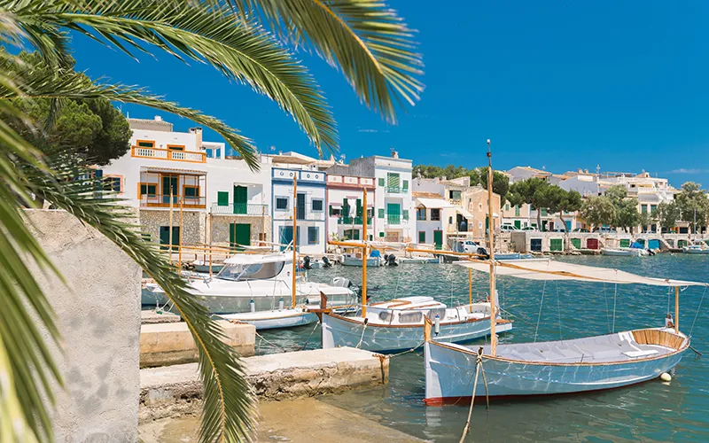 Puerto con botes y casas coloridas bajo un cielo azul brillante.