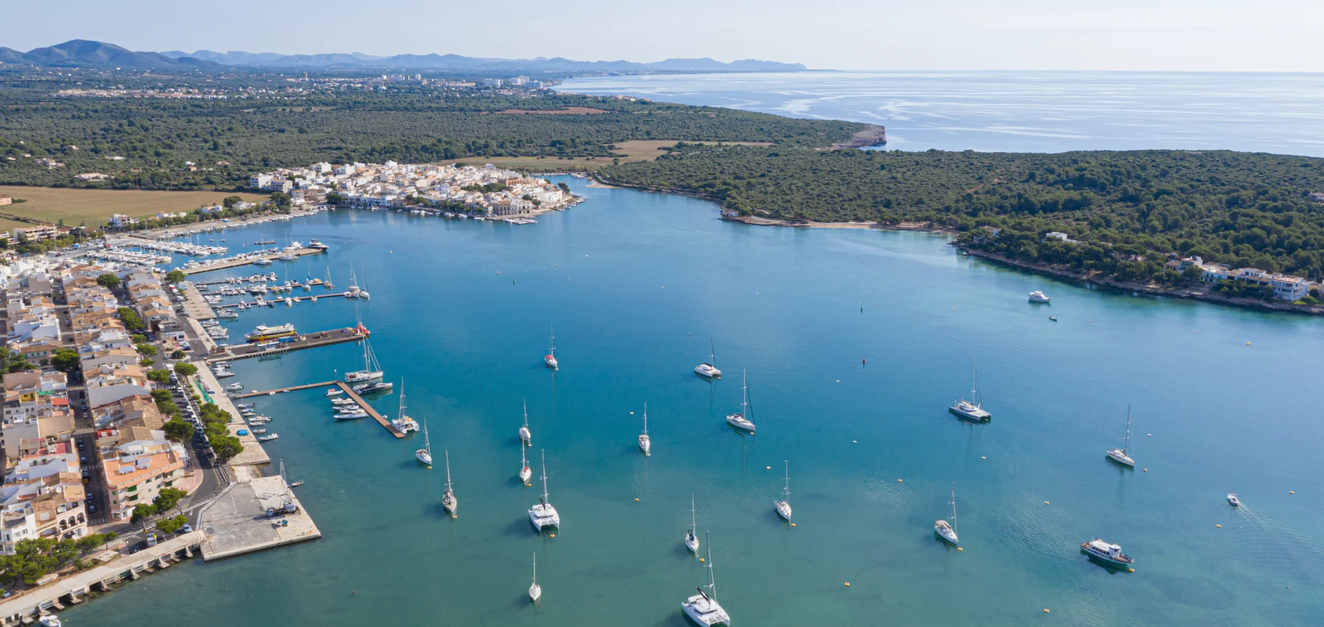 Costa con puerto, barcos y paisaje verde en el horizonte.