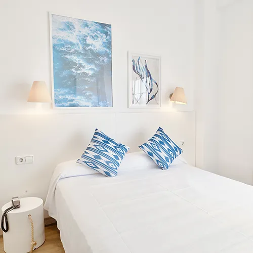 Habitaci&oacute;n blanca con dos cojines azules y cuadros de arte en la pared.