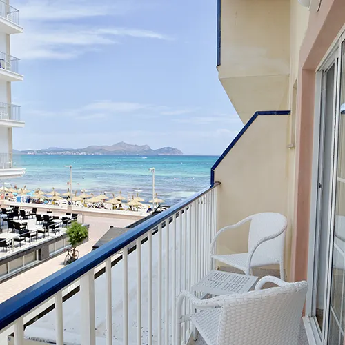 Balc&oacute;n con sillas blancas, vista al mar y playa en un d&iacute;a soleado.