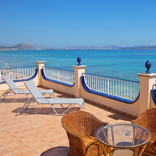 Terraza con vistas al mar, tumbonas y mesa con sillas de mimbre.
