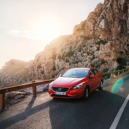 Auto rojo en carretera de monta&ntilde;a al atardecer.