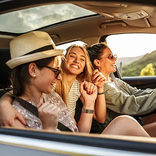 Tres amigas se r&iacute;en y disfrutan en un auto en movimiento.