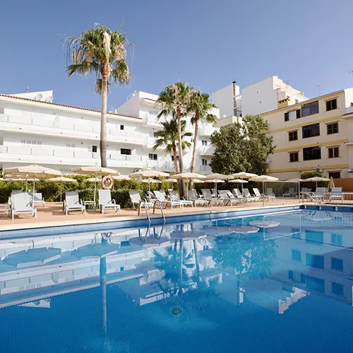 Piscina rodeada de tumbonas y palmeras, con edificios de fondo.