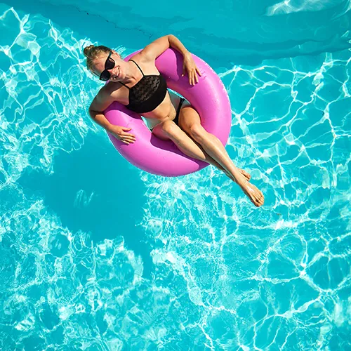 Mujer en flotador rosa en piscina con agua cristalina y luz solar.