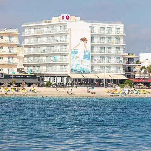 Hotel frente al mar con mural y personas en la playa.