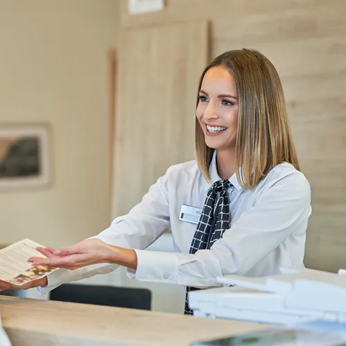 Recepcionista sonriendo mientras entrega un folleto.