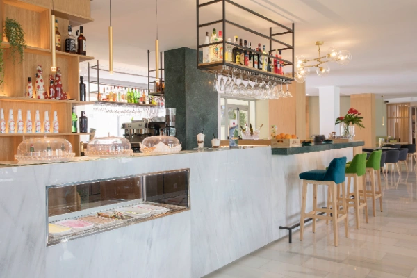 Bar moderno con sillas de colores, botellas y postres en vitrinas.