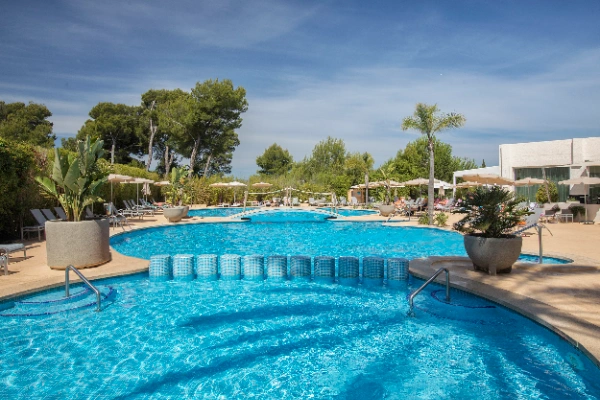 Piscina al aire libre rodeada de &aacute;rboles y tumbonas bajo un cielo despejado.