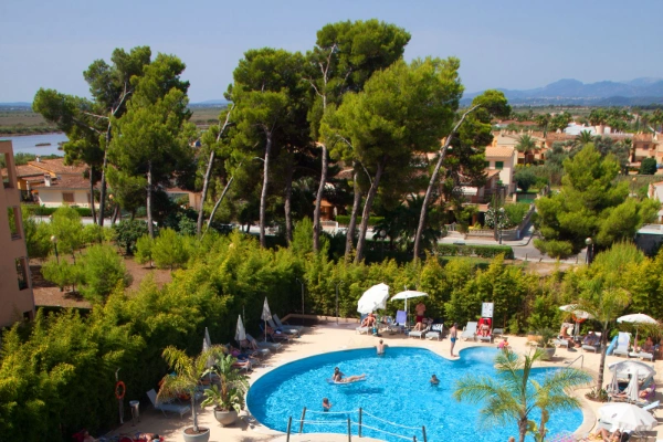 Piscina rodeada de &aacute;rboles y tumbonas en un complejo vacacional.