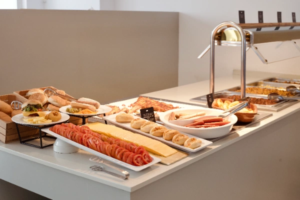 Buffet con variedad de alimentos, como embutidos, pan, y vegetales en rodajas.