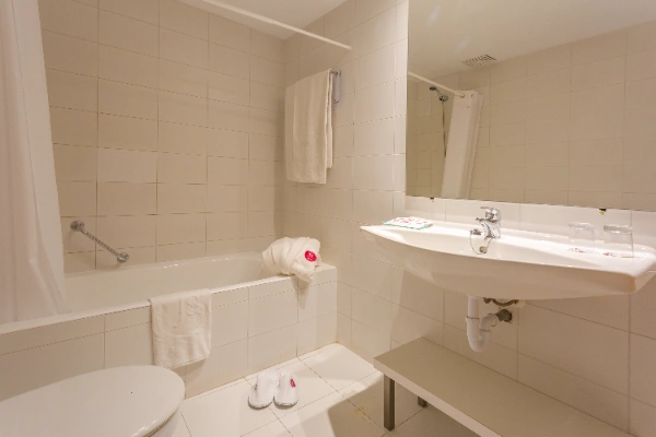 Ba&ntilde;o luminoso con ba&ntilde;era, lavabo y toallas blancas colgadas.