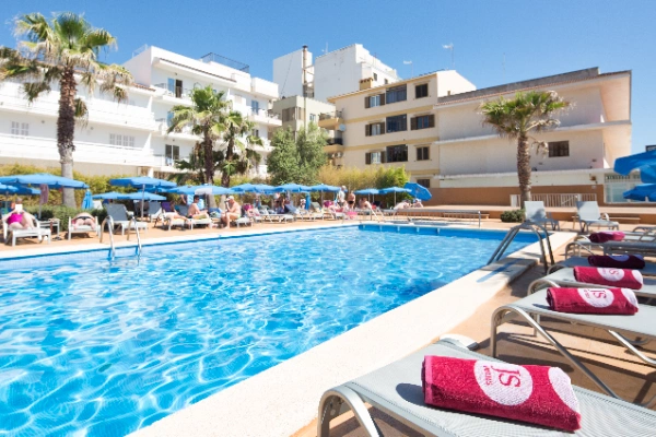 Piscina al aire libre en un hotel rodeada de tumbonas y sombrillas azules.