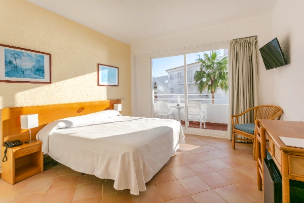 Habitaci&oacute;n luminosa con cama, balc&oacute;n, TV y muebles de madera.