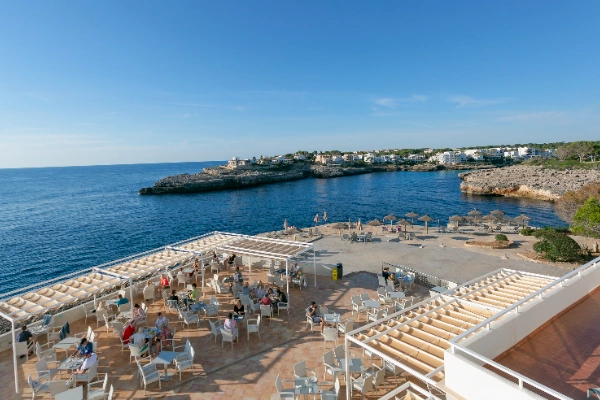 Terraza con mesas junto a un mar azul y vista de costa rocosa.