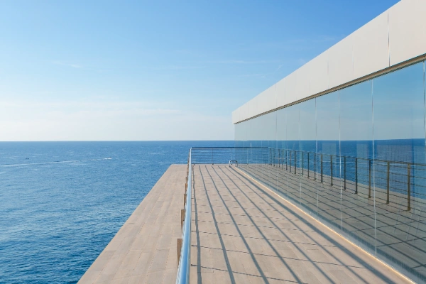 Terraza moderna con vista al mar y reflejos en vidrio.