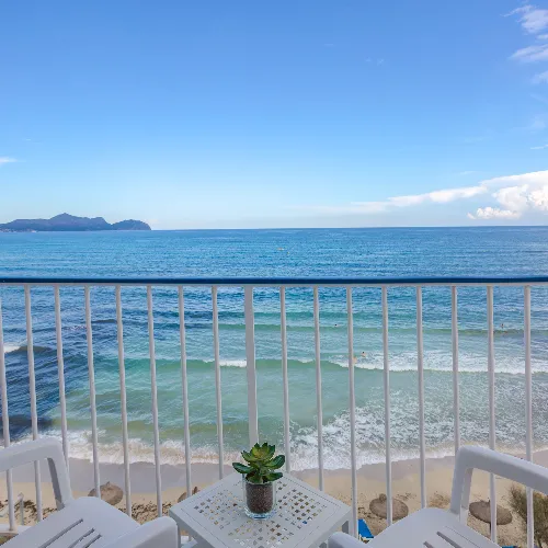 Balc&oacute;n con vista al mar, con sillas y una mesa peque&ntilde;a con planta.