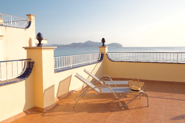 Terraza soleada con vista al mar, dos tumbonas y un sombrero.