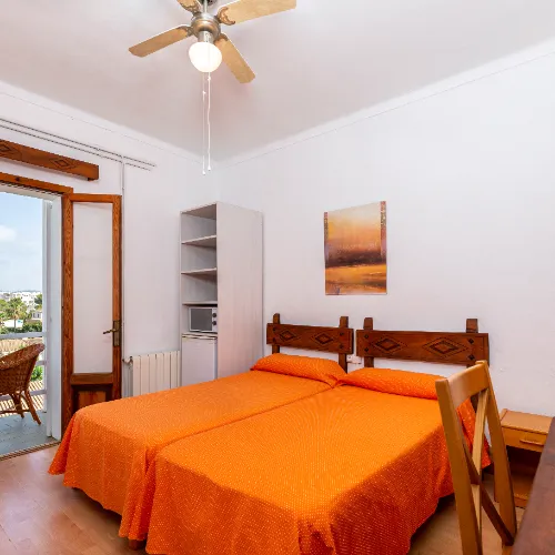 Habitaci&oacute;n con cama doble, edred&oacute;n naranja y balc&oacute;n con vista exterior.