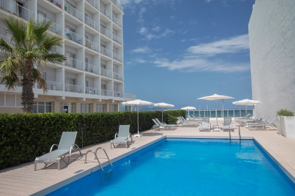 Piscina al aire libre junto a un hotel blanco y cielo despejado.