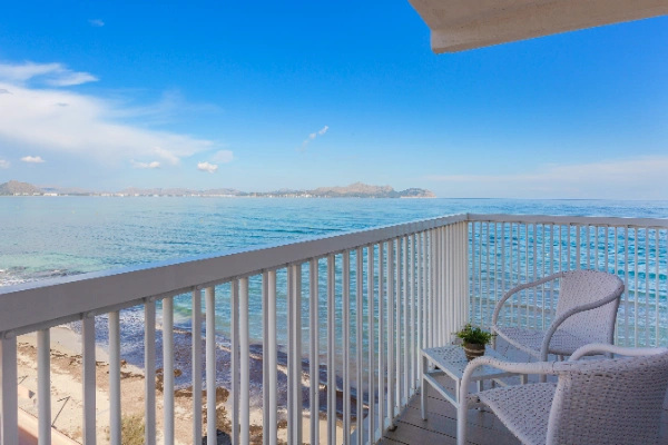 Balc&oacute;n con sillas blancas y vista al mar, cielo azul despejado.