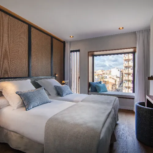 Habitaci&oacute;n de hotel con dos camas y ventana con vista a la ciudad.