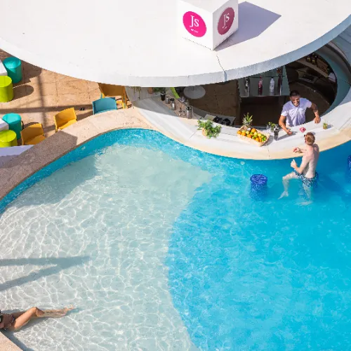 Persona en la piscina junto a un bar acu&aacute;tico con sillas amarillas y coloridas.