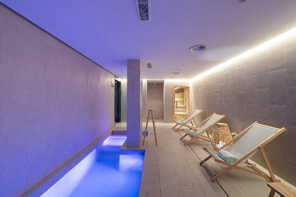 Piscina interior con tumbonas y luz ambiental en un spa moderno.