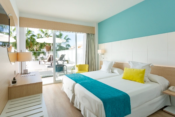 Habitaci&oacute;n moderna con camas, balc&oacute;n y vista a palmeras.