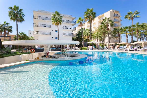 Piscina rodeada de palmeras y edificios al fondo en un d&iacute;a soleado.
