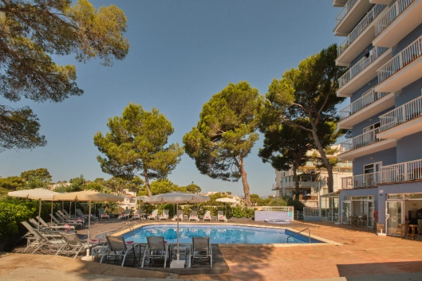 Piscina al aire libre rodeada de tumbonas y &aacute;rboles junto a un edificio.