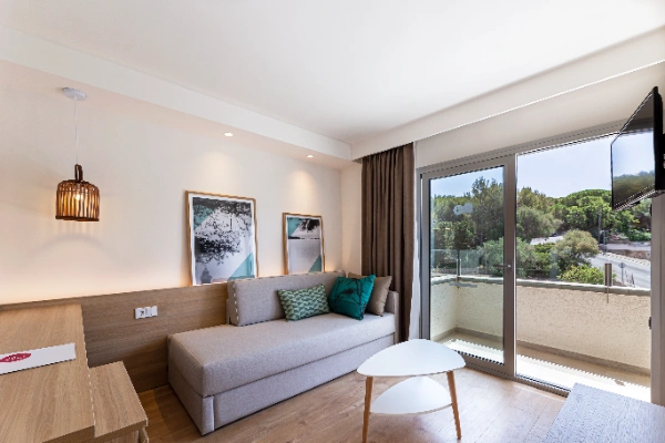 Sala moderna con sof&aacute;, mesa y vista a un balc&oacute;n con &aacute;rboles.