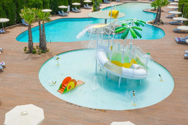 Piscina infantil con tobog&aacute;n acu&aacute;tico y palmera, rodeada de tumbonas.