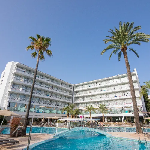 Hotel moderno con piscina y palmeras bajo el cielo azul.