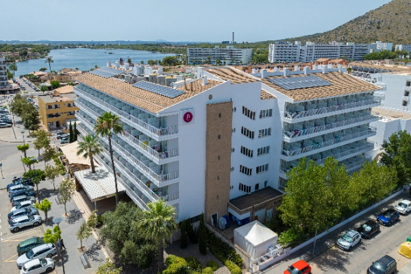 Edificio de apartamentos con paneles solares, cerca de un lago y colina al fondo.