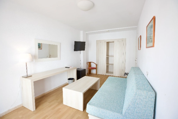 Sala minimalista con sof&aacute; azul, televisor y escritorio de madera clara.