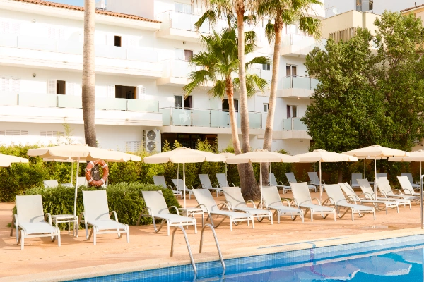 Piscina con tumbonas y sombrillas frente a un edificio de apartamentos.