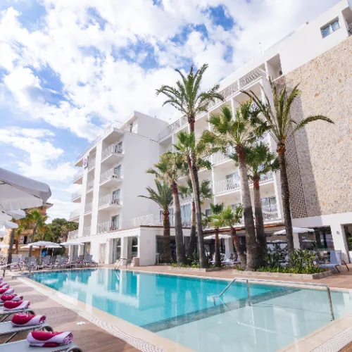 Hotel con piscina y palmeras bajo un cielo azul.