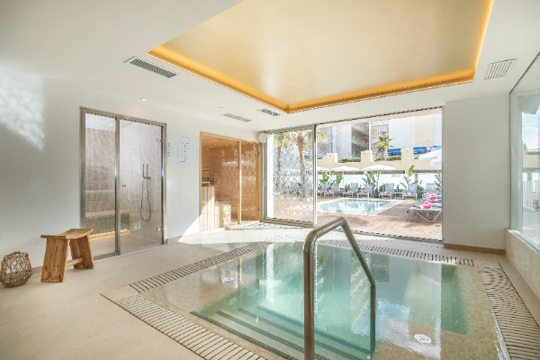 Piscina interior moderna con acceso a terraza soleada y puerta de cristal.