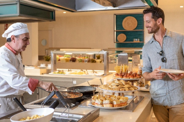 Chef cocinando en buffet, hombre elige comida en plato.