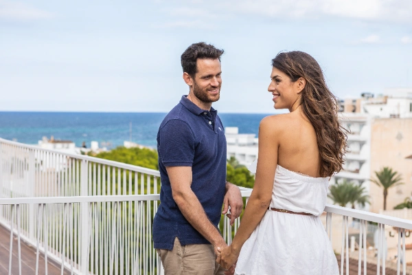 Pareja sonriendo en una terraza con vista al mar.