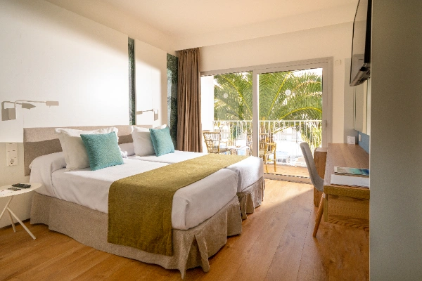 Habitaci&oacute;n de hotel con cama doble, terraza y vista a las palmeras.