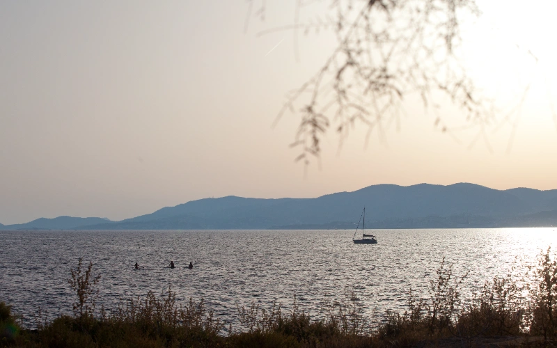 Mar, bote, monta&ntilde;as y nadadores al atardecer.