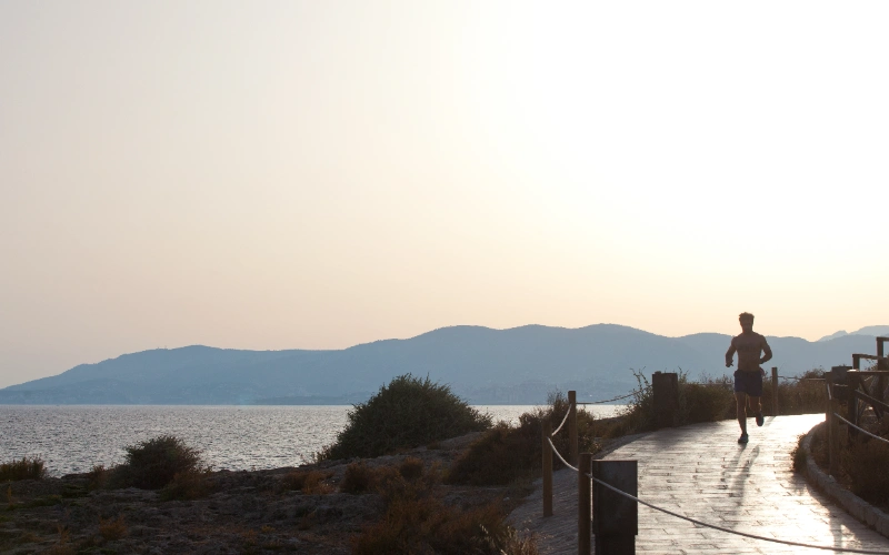 Persona corriendo cerca del mar, con monta&ntilde;as al fondo al atardecer.