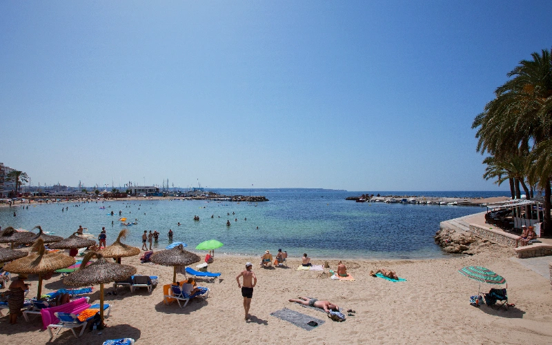 Playa soleada con sombrillas, turistas en la arena y el mar en el horizonte.